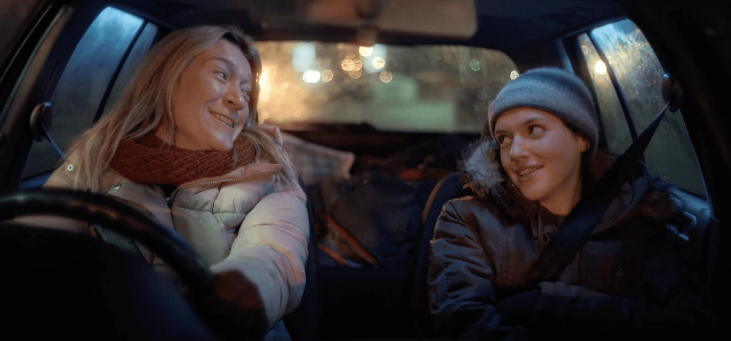 A mother and daughter sat in a car wearing winter coats, hats and scarves