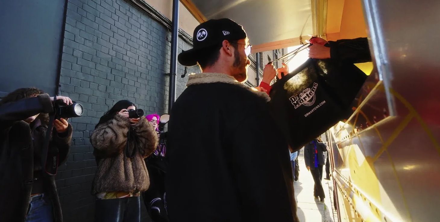 A man being handed a black Dr. Martens bag from a van 