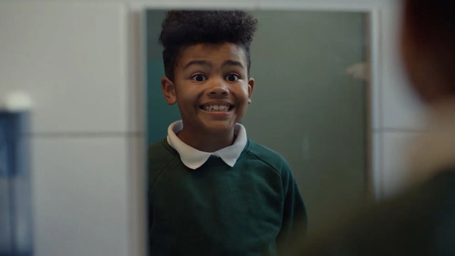 A young boy forcing a smile in a mirror in Shelter’s emotional advertising campaign