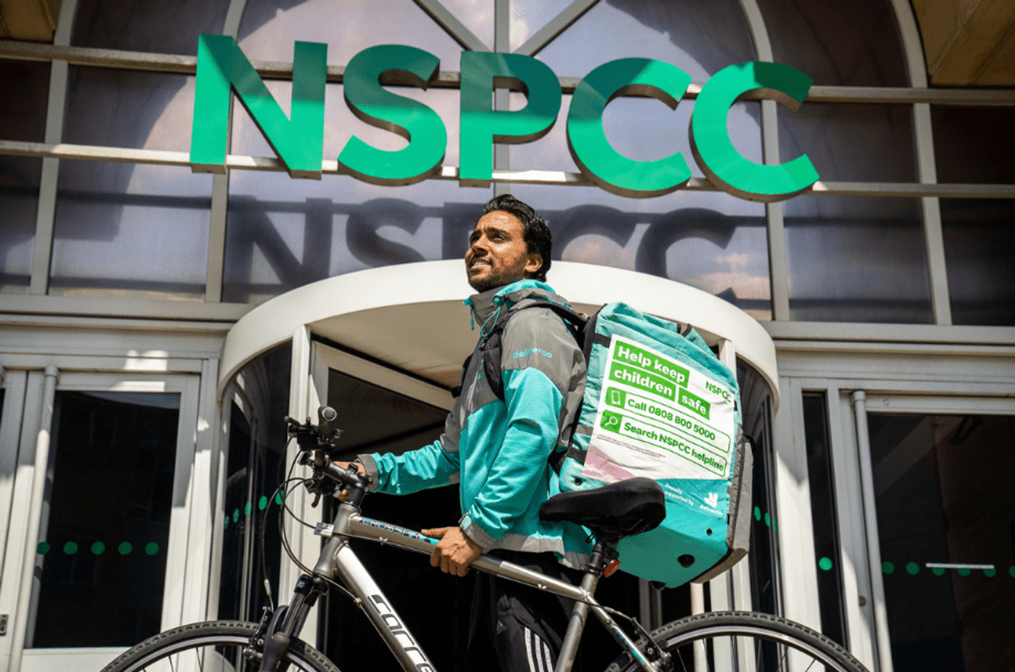 A man wearing a Deliveroo uniform with his bike outside NSPCC head office