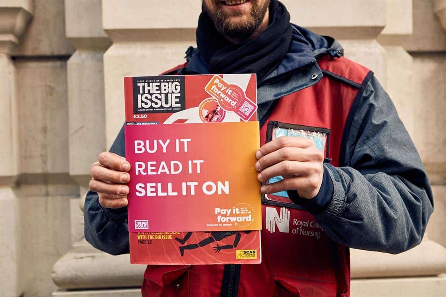 A man smiling holding an issue of The Big Issue magazine