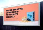 Surreal cereal billboard claiming Dwayne Johnson's a fan, with a footnote he's a bus driver from London