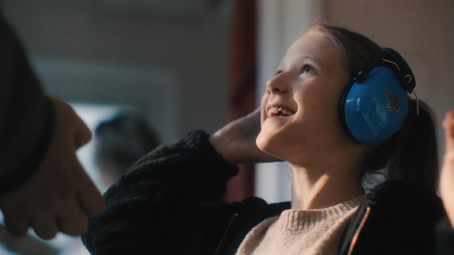Penny, wearing blue ear defenders, smiles up at her father Chris in Don't Panic London's 
