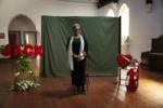 An elderly woman standing in front of red memorial flowers for her late husband