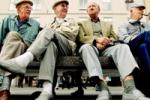 Four elderly men sat on a bench talking and laughing