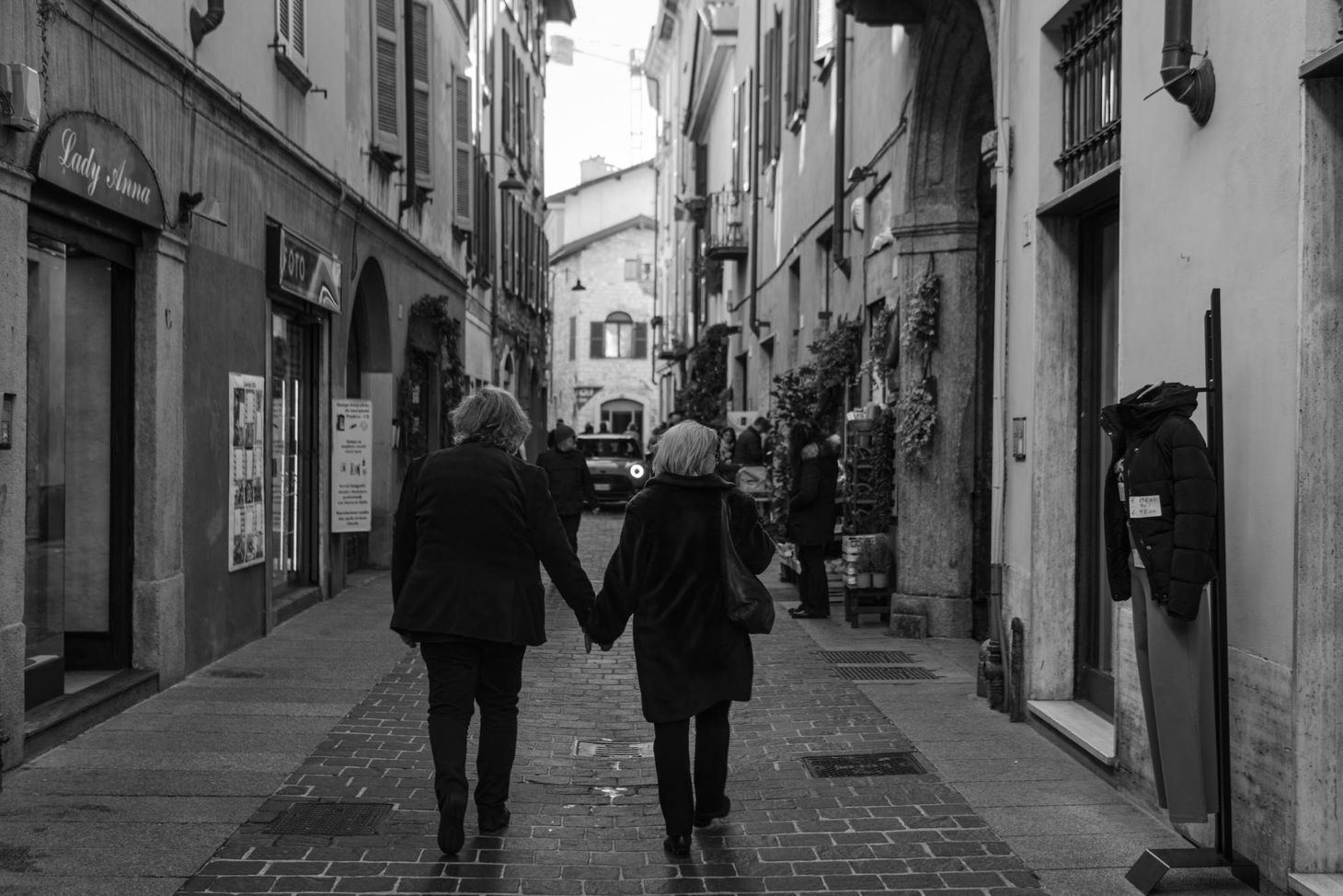 An older couple holding hands walking down an Italian street