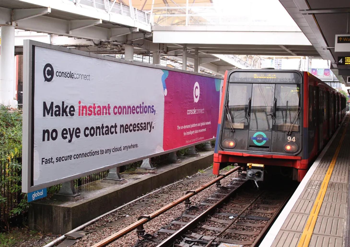 Console Connect billboard beside a DLR train in London reading 'Make instant connections, no eye contact necessary'.