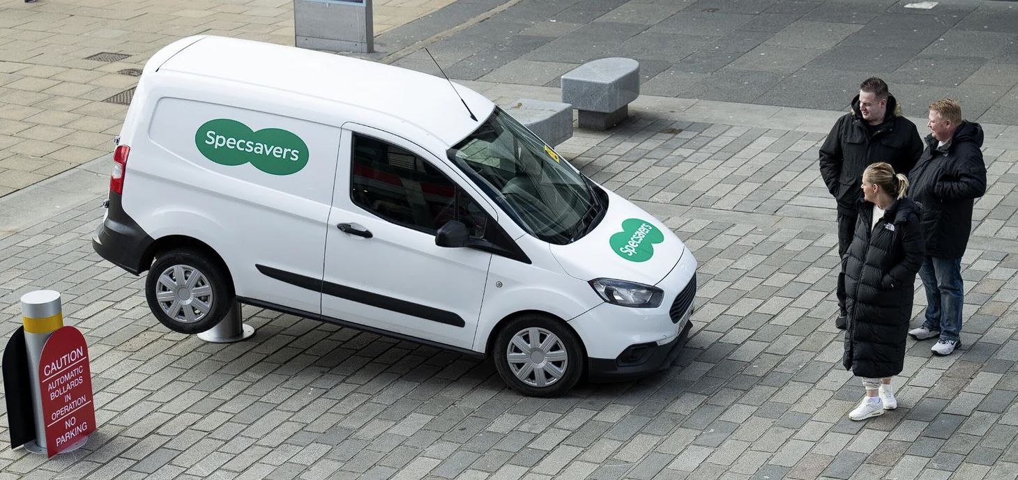  A white Specsavers-branded van with its back end lifted up by a bollard, next to a red warning sign