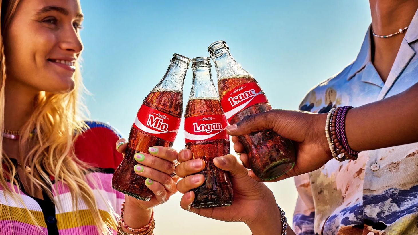 A young woman smiles as she toasts her friends with Coke bottles with their names on in Coca-Cola’s emotional advertising campaign