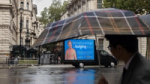 Don't Panic London's OilyFans ad van, with the satirical billboard, driving in the rain past the gates of Downing Street in London, protesting oil executive profits.