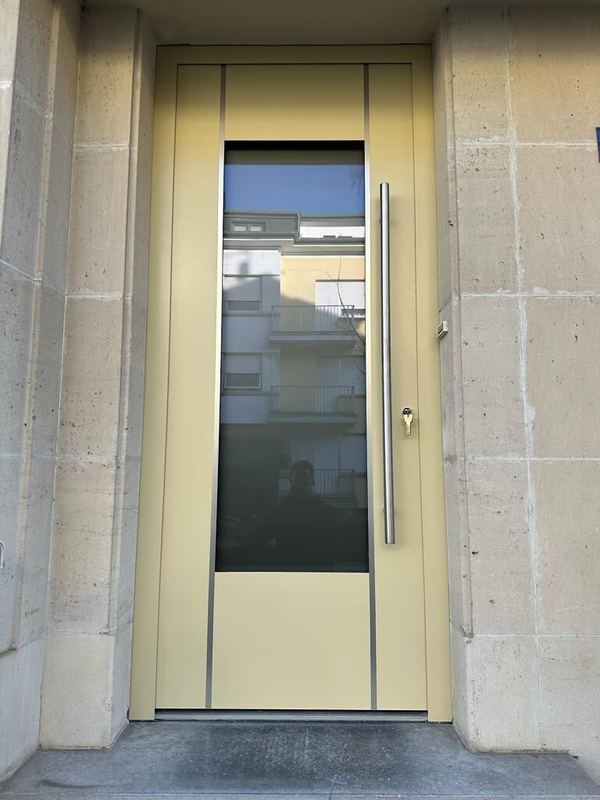 Blassgelbe Haustür frontal, großes dunkles Glasfeld und Stangengriff, Fassade aus Werkstein