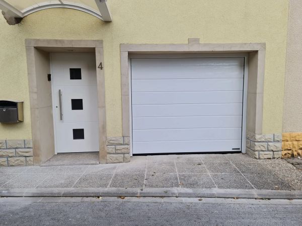 Weißes Sektionaltor neben einer weißen Haustür mit drei quadratischen Glaseinsätzen