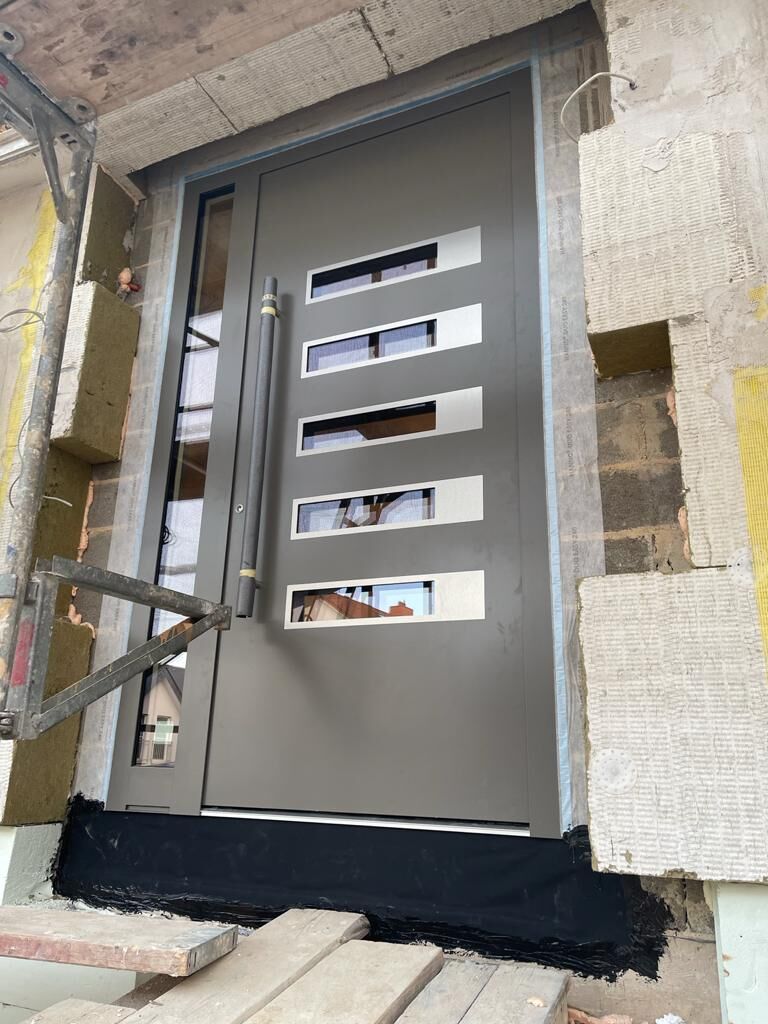 Dunkelgraue Haustür mit fünf waagerechten Glasstreifen in Edelstahlrahmen und Seitenteil auf der Baustelle
