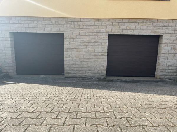 Zwei dunkelbraune Sektionaltore in einer hellen Betonstein-Fassade