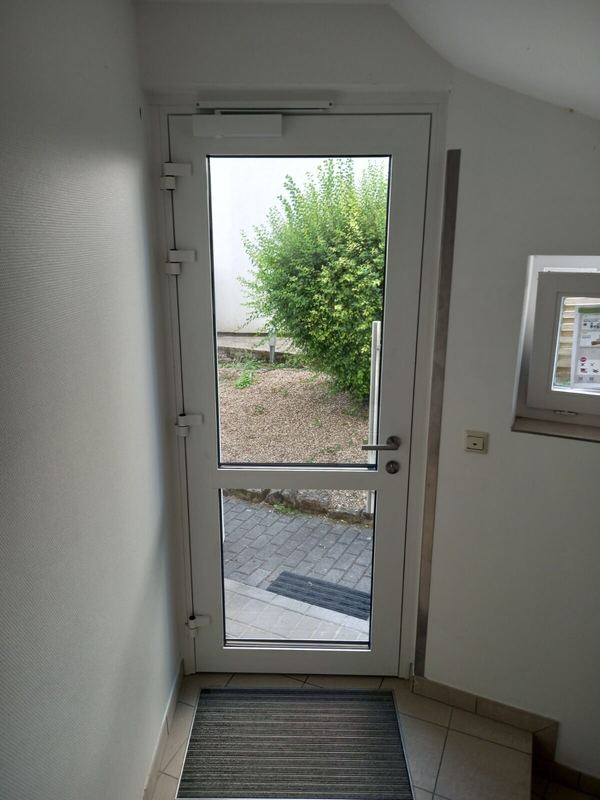 Weiße Aluminium-Nebeneingangstür mit zwei Klarglasfeldern und Türschließer, Blick von innen in den Garten