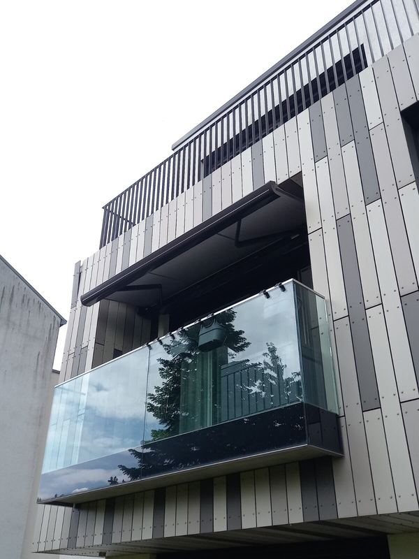 Dunkle Markise über einem Glasbalkon an Gebäude mit vertikaler Fassadenverkleidung