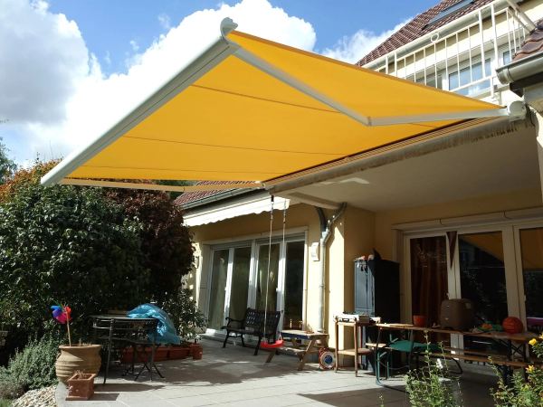 Gelb-orange Gelenkarmmarkise über einer Familienterrasse mit Schaukel
