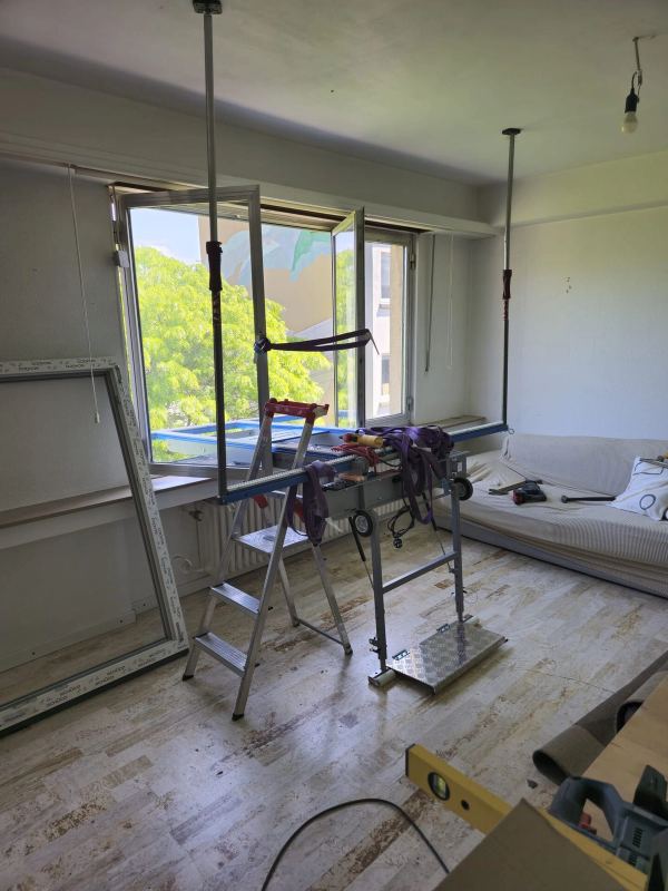 Fenstertausch in einer Wohnung, alter Rahmen auf einem Montagegerät und neuer weißer Rahmen an der Wand