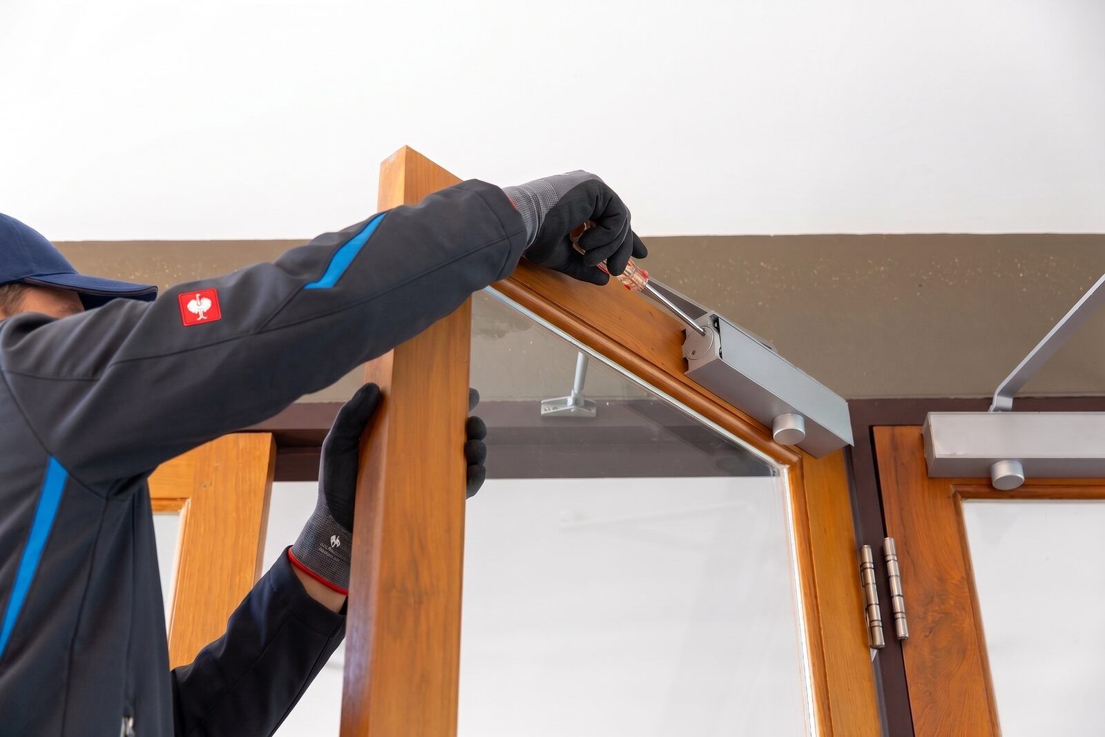 Techniker stellt mit dem Schraubendreher den Türschließer oben an einer verglasten Holzrahmentür ein