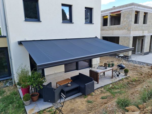 Große anthrazit Markise über Terrasse eines Neubaus neben einer Baustelle