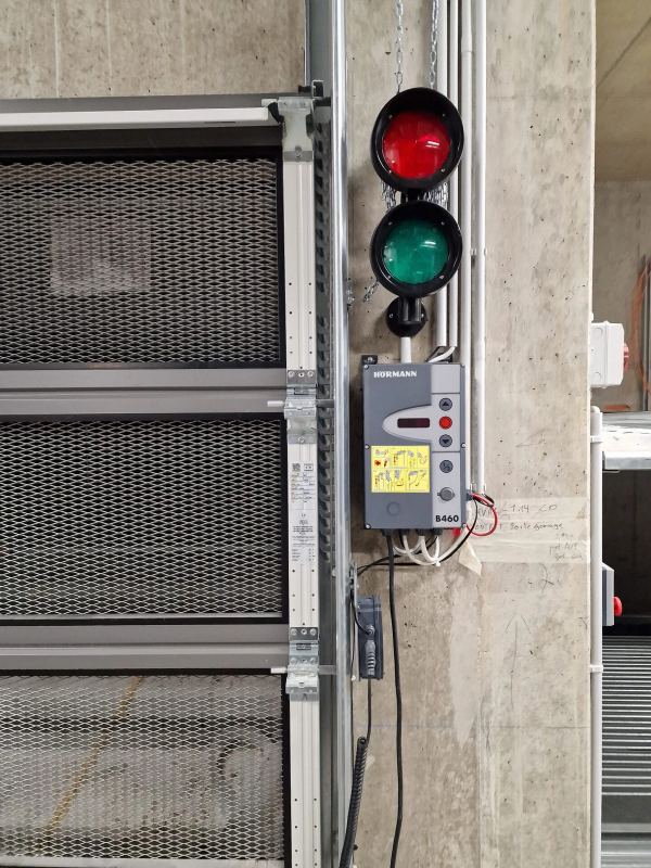 Hörmann-Steuerung B460 mit Rot-Grün-Ampel neben einem Industrietor mit Gitterfüllungen