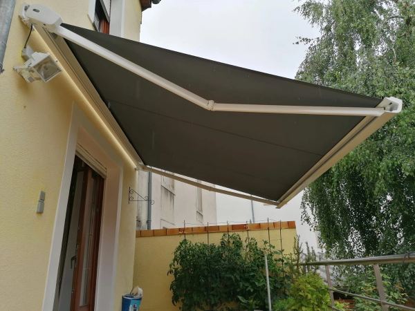 Markise mit olivgrünem Tuch und weißem Gestell an gelbem Haus