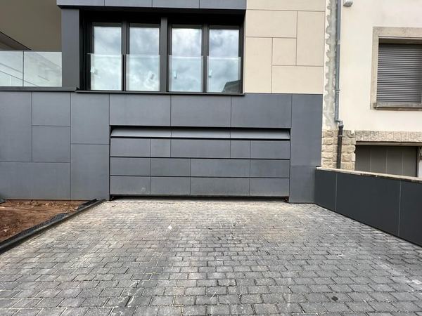 Flächenbündiges Garagentor, verkleidet mit denselben grauen Platten wie die moderne Fassade