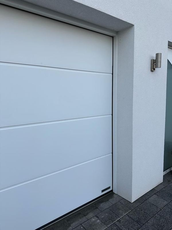 Nahaufnahme eines weißen Hörmann-Sektionaltors an moderner weißer Fassade mit Edelstahlleuchte