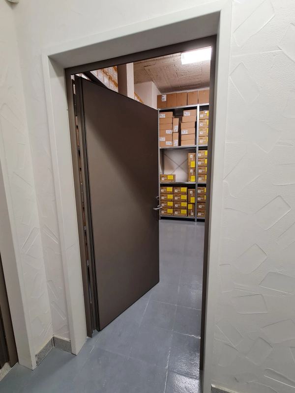 Offene dunkelbraune Stahltür zu einem Archivraum mit Regalen voller Kartons