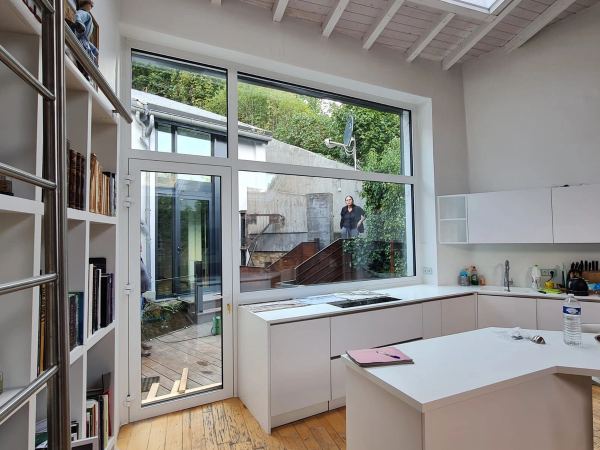 Große weiße Fensterwand mit Tür zum Innenhof, gesehen aus einer weißen Küche mit offenem Dachstuhl