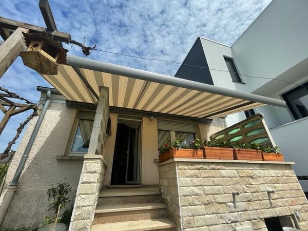 Beige-taupe gestreifte Markise über einem bepflanzten Steinpodest mit Treppe