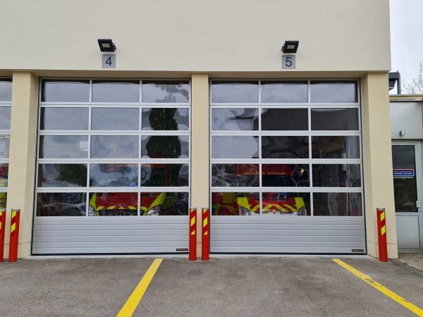 Zwei verglaste Aluminium-Sektionaltore einer Feuerwache, Einsatzfahrzeuge dahinter sichtbar