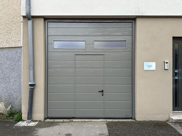 Frontansicht eines grauen Sektionaltors mit mittiger Schlupftür und zwei Milchglasfenstern