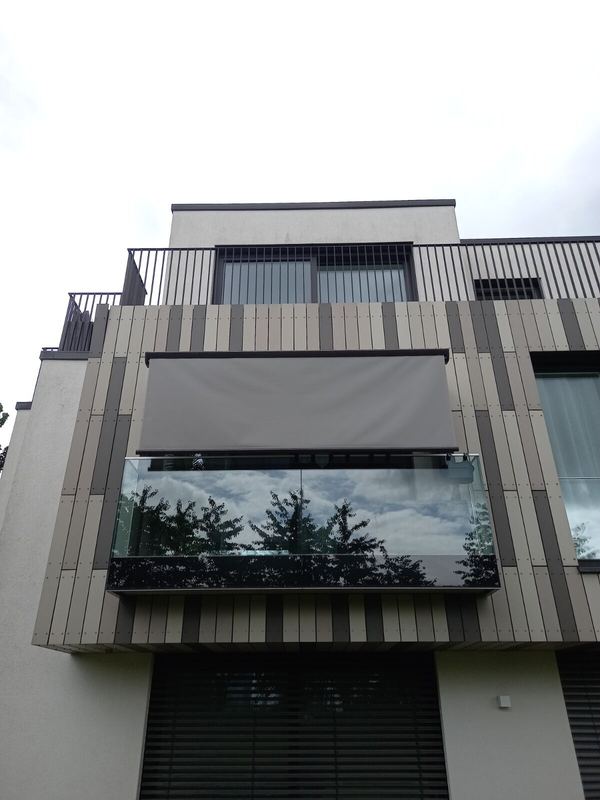 Graue Markise ausgefahren über Glasbalkon, Frontansicht eines verkleideten Gebäudes
