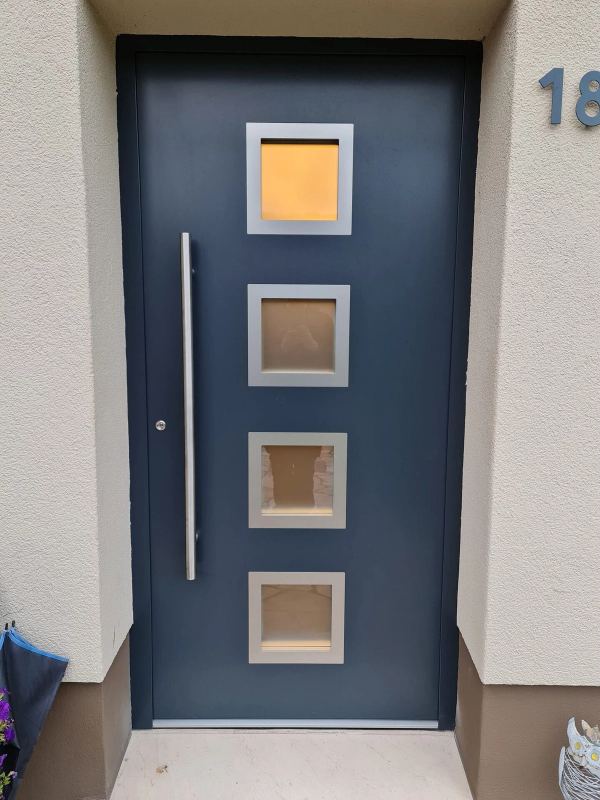 Blaugraue Haustür mit vier quadratischen Glasfeldern in Edelstahlrahmen und Stangengriff