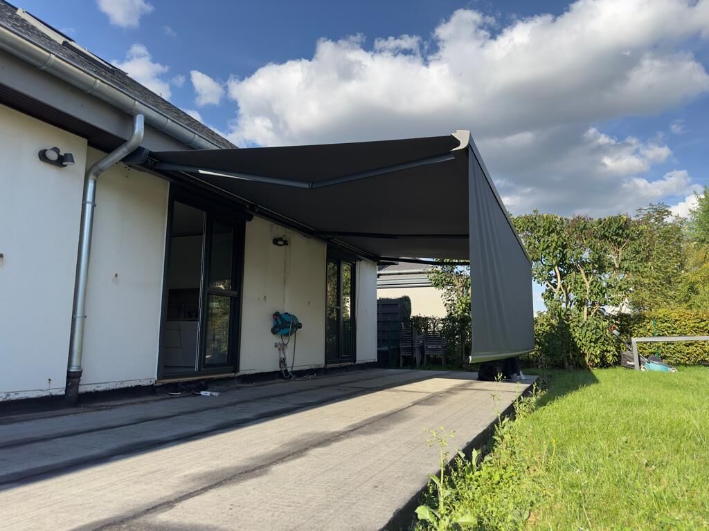 Anthrazit Markise mit ausgefahrenem Volant am weißen Bungalow mit Rasen