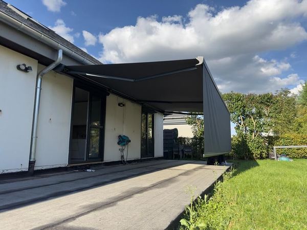 Anthrazit Markise mit ausgefahrenem Volant am weißen Bungalow mit Rasen
