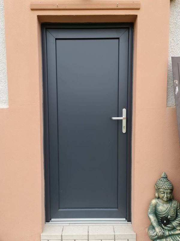 Anthrazitfarbene Nebeneingangstür mit glatter Füllung und Edelstahldrücker, lachsfarbener Putz, Buddha-Figur
