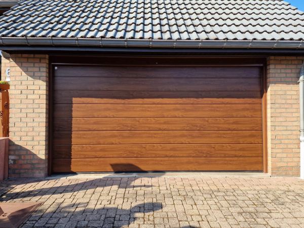 Breites Sektionaltor in dunkler Eichenoptik an einem Klinkerhaus mit Ziegeldach