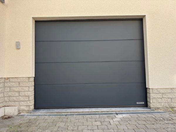 Glattes anthrazitfarbenes Hörmann-Sektionaltor mit 4 Paneelen, cremefarbene Fassade mit Steinsockel