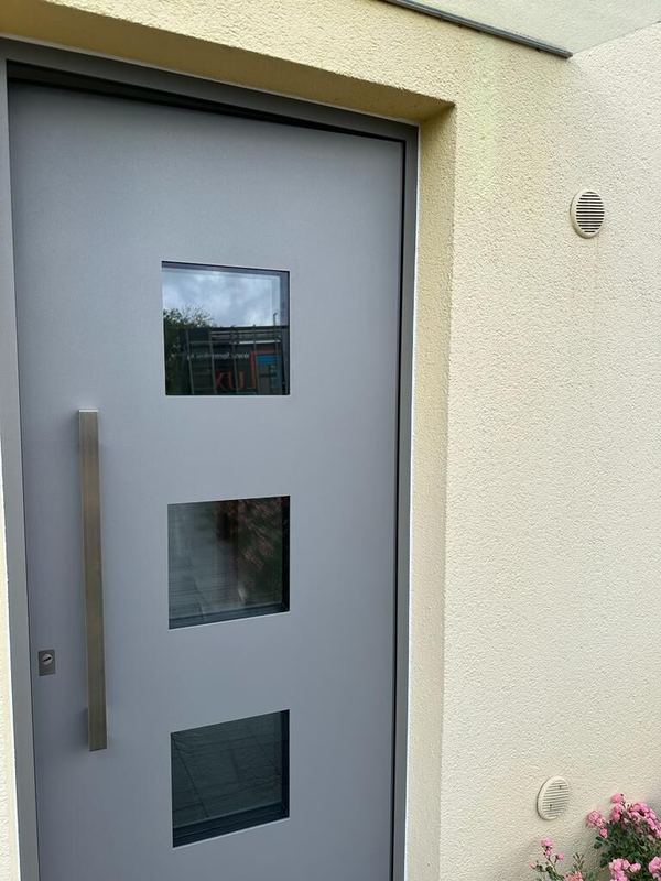 Hellgraue Haustür mit drei quadratischen Glasfeldern und Vierkantgriff, schräg gesehen, rosa Rosen