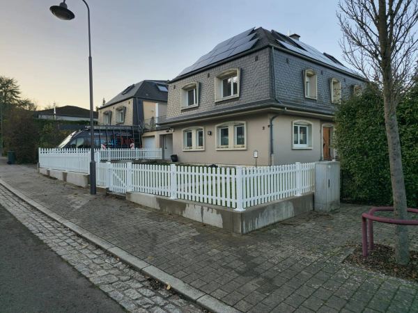 Weißer Lattenzaun mit passender Gartentür auf Sockelmauer, Haus mit Schieferdach und Solarmodulen