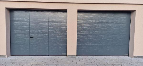Zwei anthrazitfarbene Sektionaltore nebeneinander, eines mit Schlupftür, beige Putzfassade