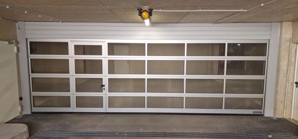 Breites Sektionaltor mit Aluminiumrahmen, Gitterfüllung und Schlupftür in einer Tiefgarage