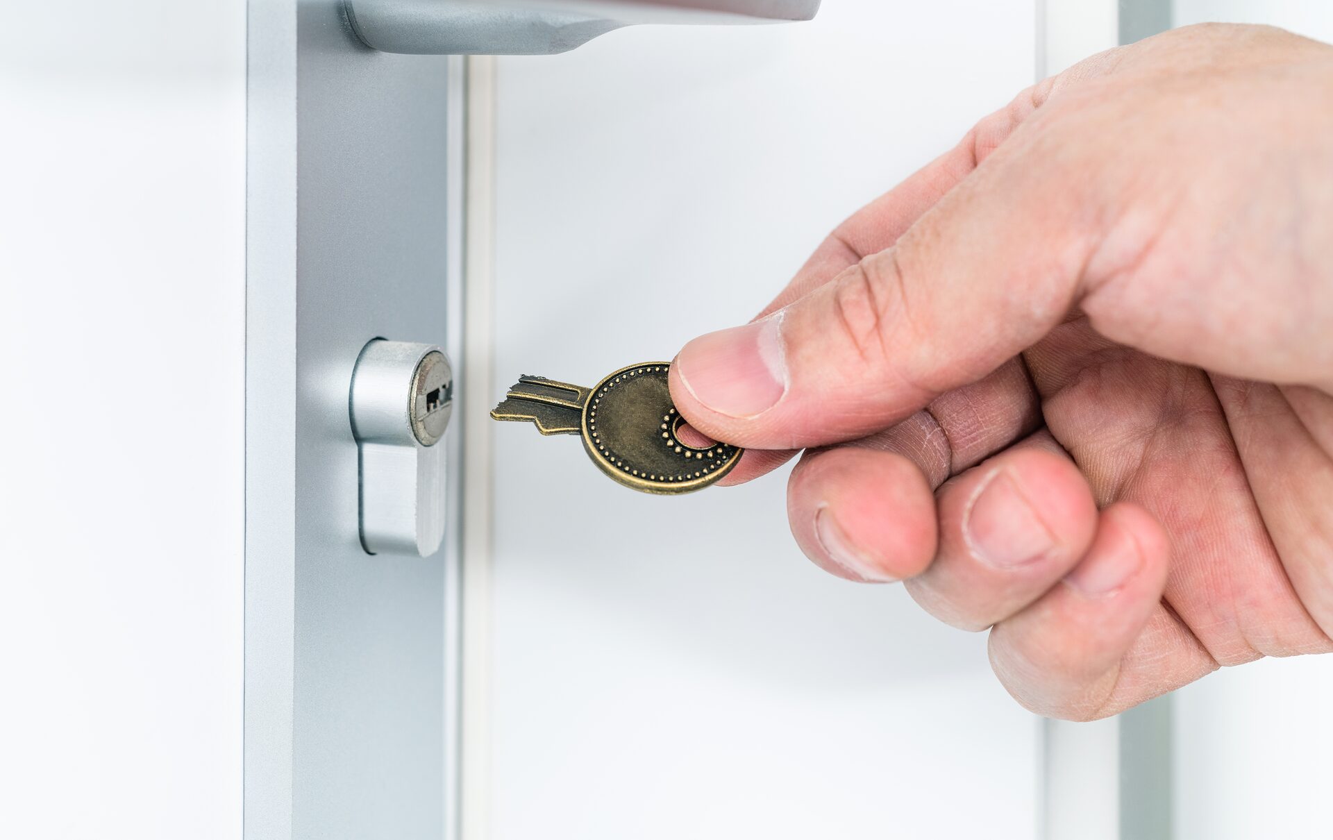 Hand mit einem Schlüssel vor dem Schließzylinder einer hellgrauen Aluminium-Haustür
