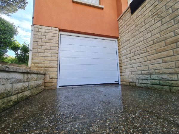 Weißes Sektionaltor aus der Froschperspektive, orange Fassade, Natursteinmauern, Waschbetonboden