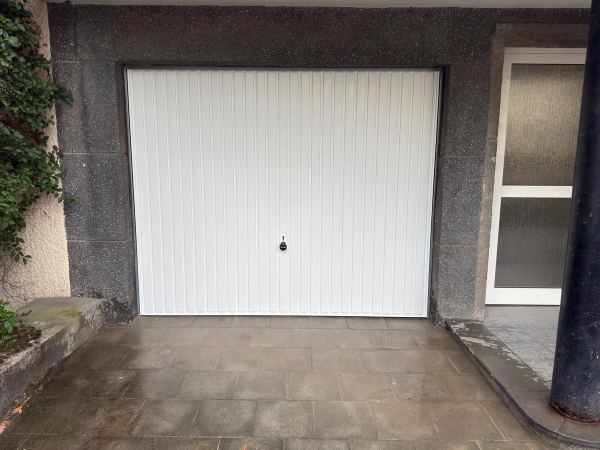 Weißes Schwingtor mit senkrechten Sicken, Granitfassade neben verglaster Eingangstür