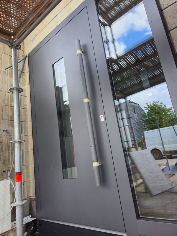 Dunkelgraue Haustür mit schmalem Glas und großem Glasseitenteil, Griff noch geschützt, auf der Baustelle