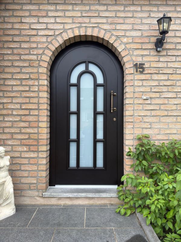 Dunkelbraune Rundbogen-Haustür mit Sprossenverglasung und Bronzegriff in heller Klinkerfassade