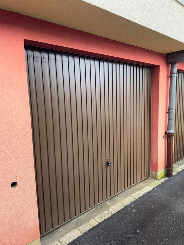 Braunes Schwingtor mit senkrechten Sicken in einer Garagenreihe mit rosa Fassade